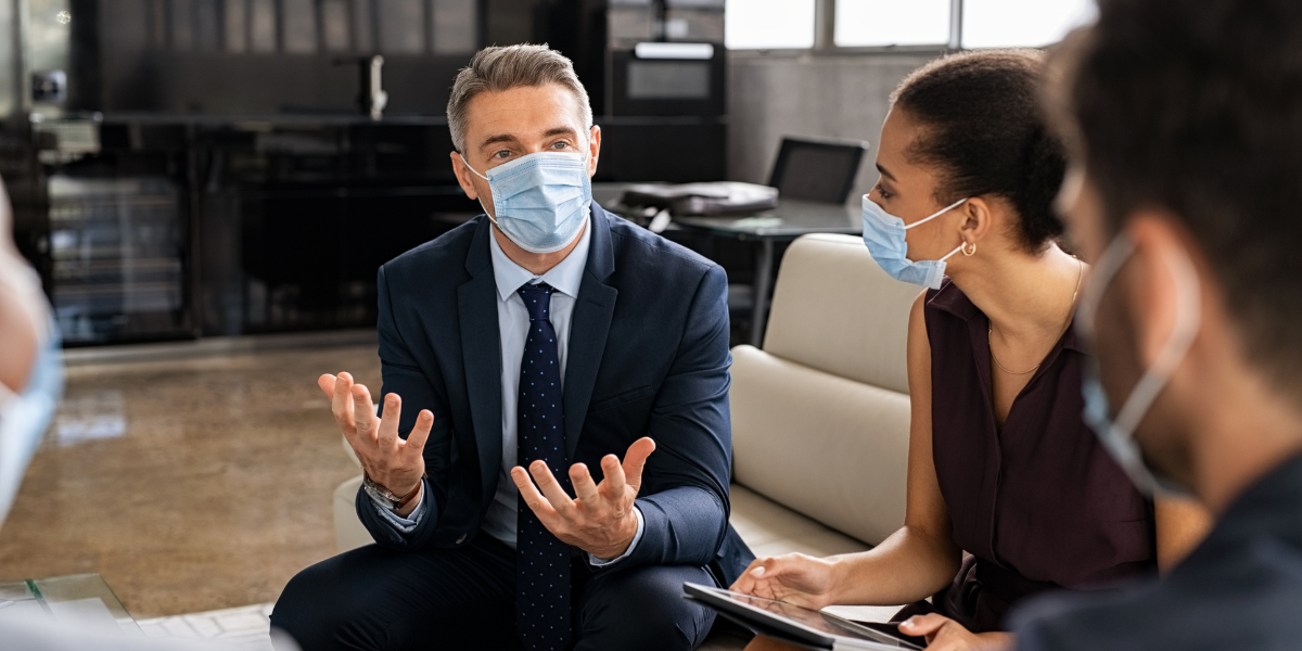 Team of entrepreneurs wearing protective face masks while talking about business reports on a meeting during coronavirus epidemic.