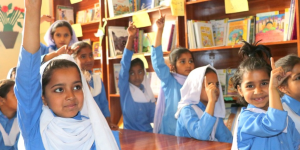 Young girls excitedly raise their hands to answer a question while learning in schools supported by DIL
