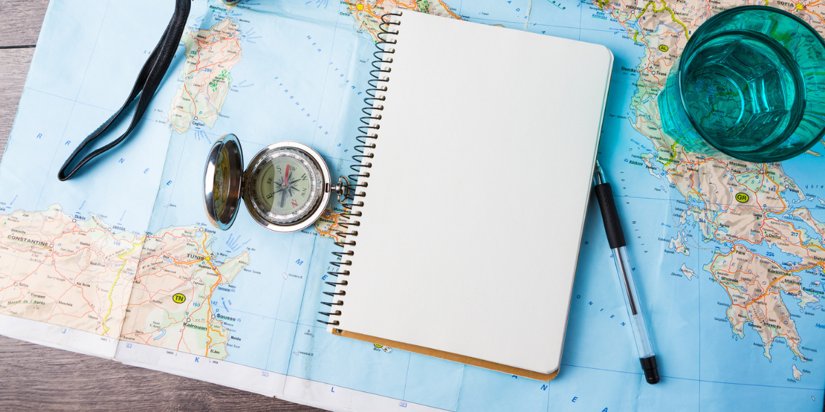 A compass, a notebook, a pen and a cup, sitting atop a map of the world - 4 Questions you Should Consider Before Giving Abroad